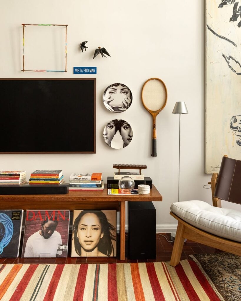 Rack de madeira com livros e discos, tapete listrado, pratos em branco e preto na parede
