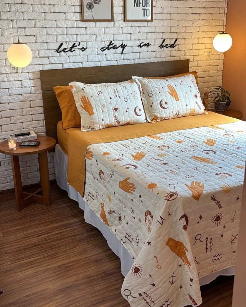 Quarto com cabeceira de madeira, colcha e almofadas com mãos, luas e estrelas