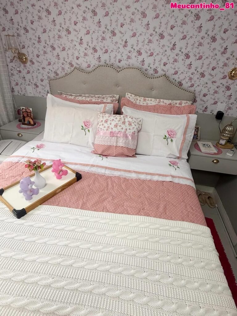 Quarto com papel de parede floral, travesseiros brancos com rosa e manta rosa