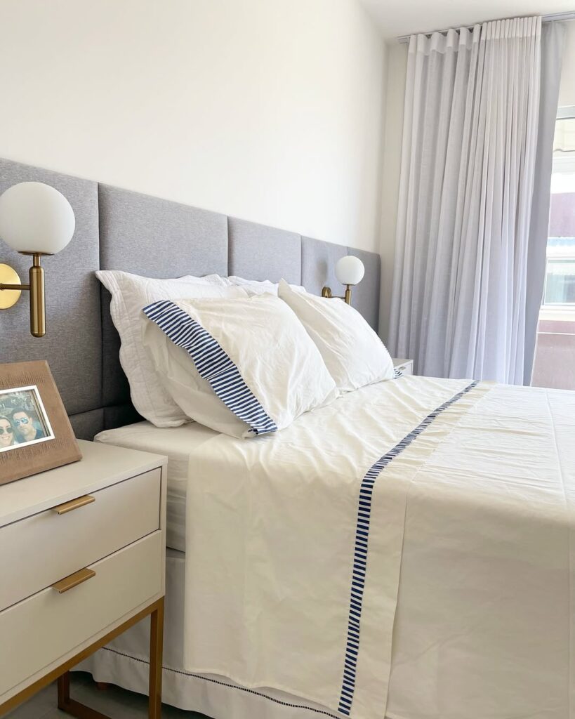 Quarto com cabeceira estofada modular cinza, e roupa de cama branca