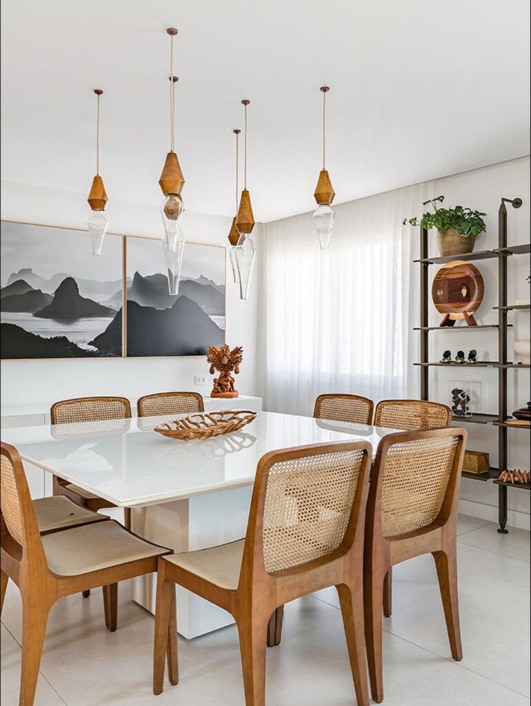 Sala de jantar com mesa branca, cadeiras com palhinha no encosto e pendentes