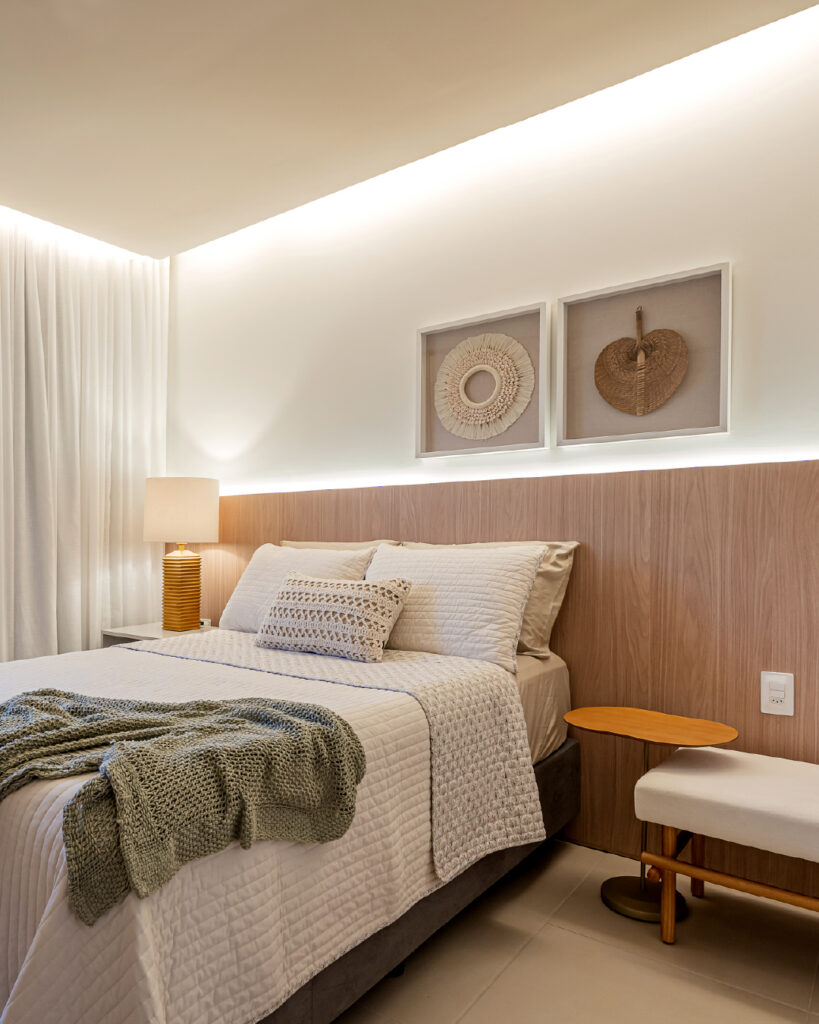 Quarto em cores neutras com quadros na parede, manta e almofadas na cama