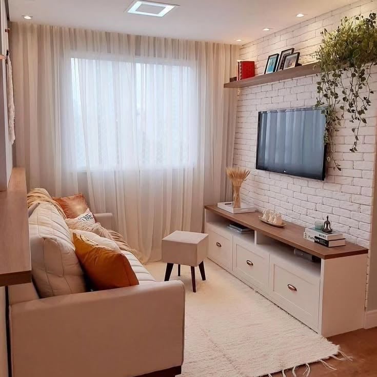 Sala pequena em tons claros, com parede de tijolinho atrás da tv e rack com gavetas