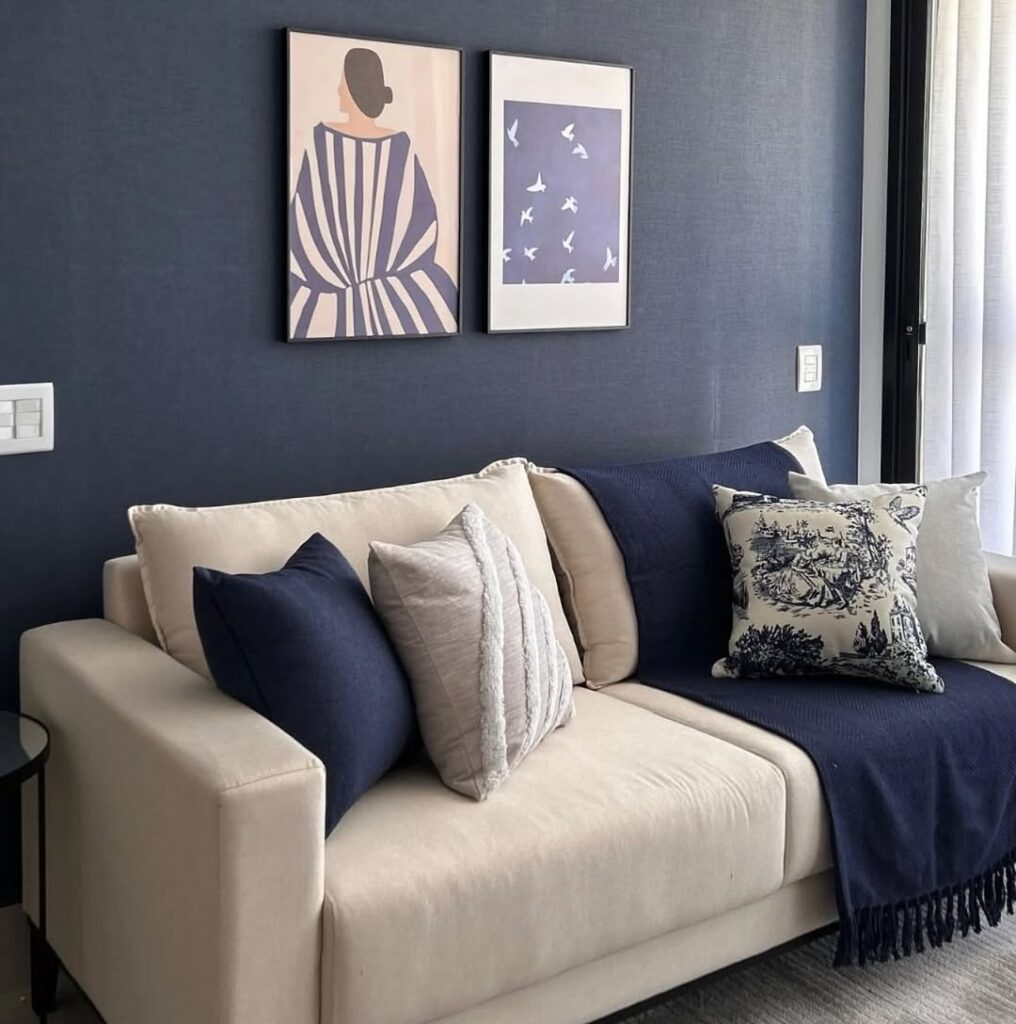 Sala de estar com sofá bege, almofadas e parede em azul escuro