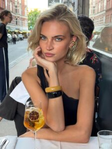Mulher de pele clara, com look preto e cabelo loiro blunt bob