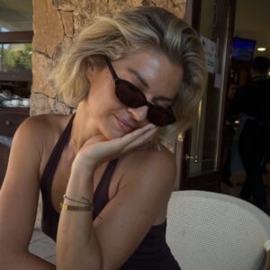 Mulher de pele clara, com regata, óculos escuros e cabeo curto loiro