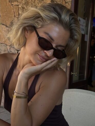 Mulher de pele clara, com regata, óculos escuros e cabeo curto loiro