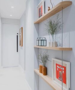 Corredor branco com prateleiras estreitas de madeira, vasinhos e quadros decorativos