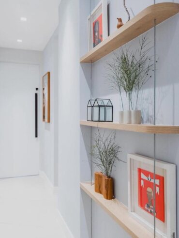 Corredor branco com prateleiras estreitas de madeira, vasinhos e quadros decorativos