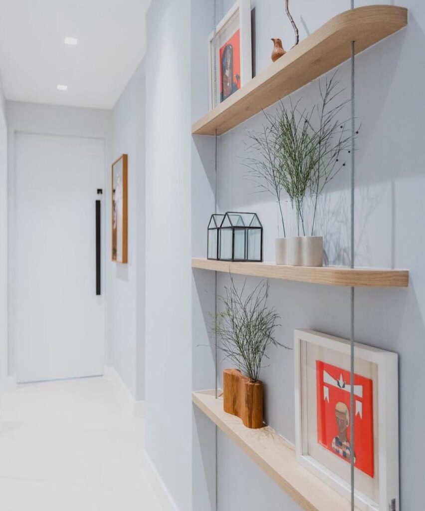 Corredor branco com prateleiras estreitas de madeira, vasinhos e quadros decorativos