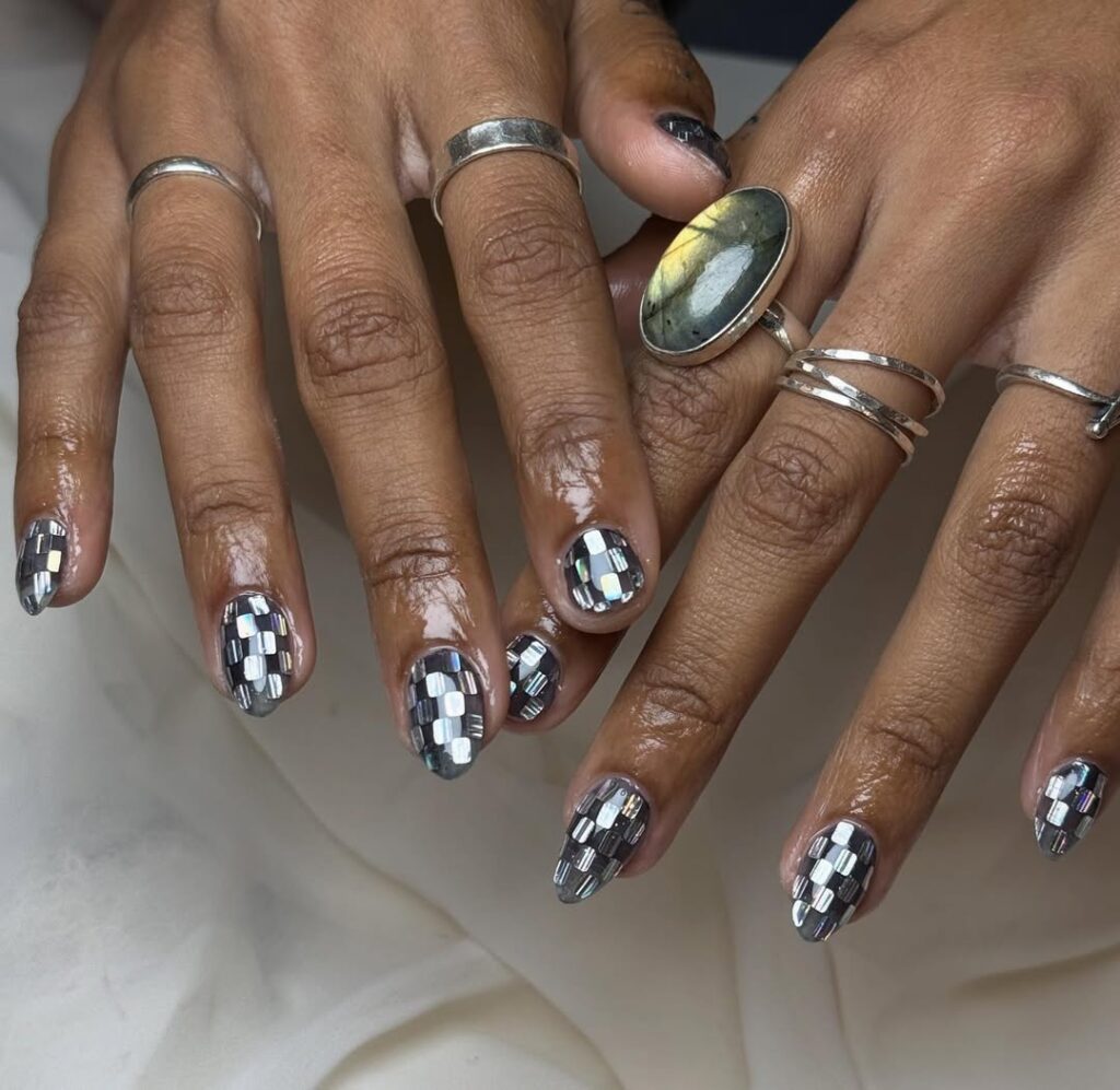 Mãos de pele preta, com anéis em prata e unha amendoada decorada estilo disco 