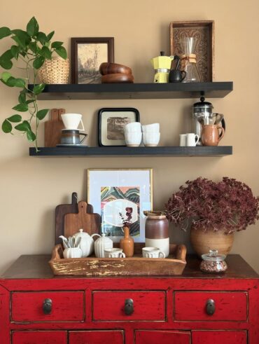 Balcão vermelho de madeira com prateleiras abertas, xícaras e cafeteiras