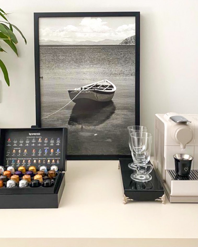Bancada com itens de café e quadro com moldura preta e foto de um barco no mar