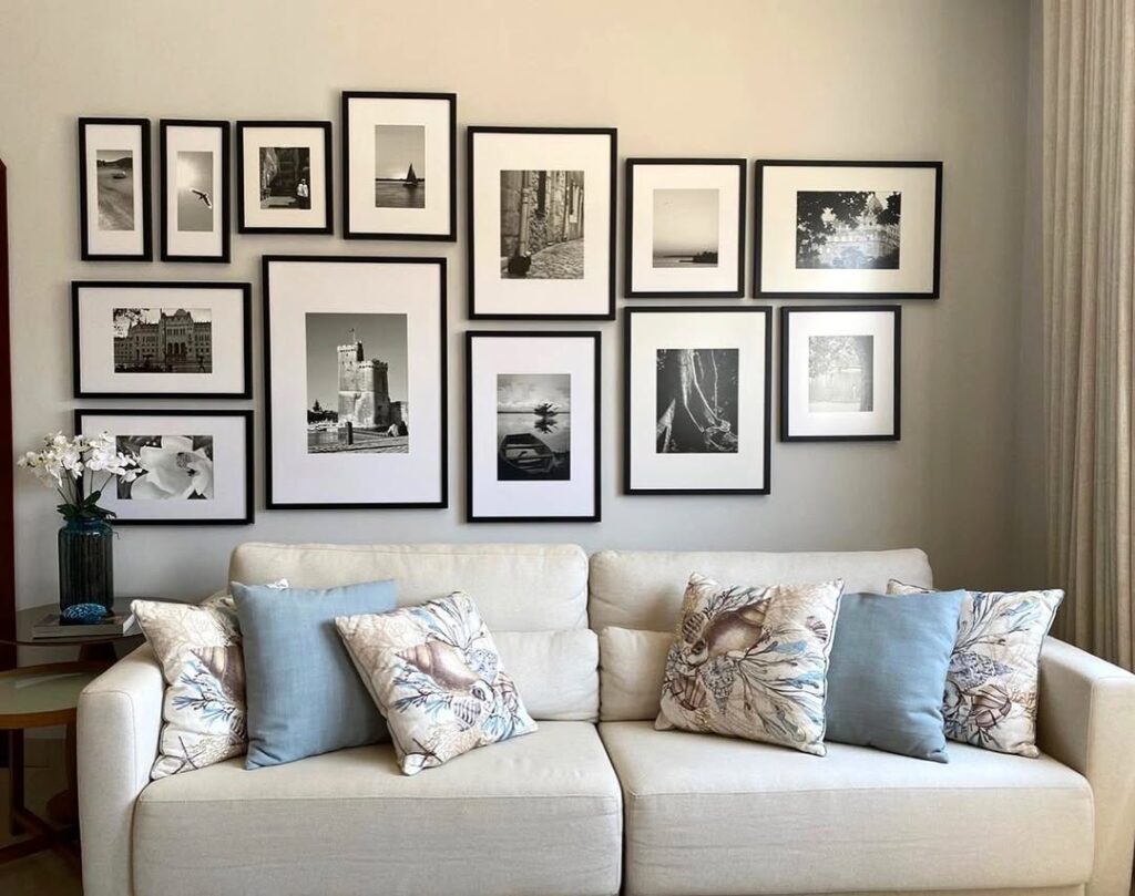 Sala de estar com sofá claro, almofadas e galeria de quadros com fotos em preto e branco