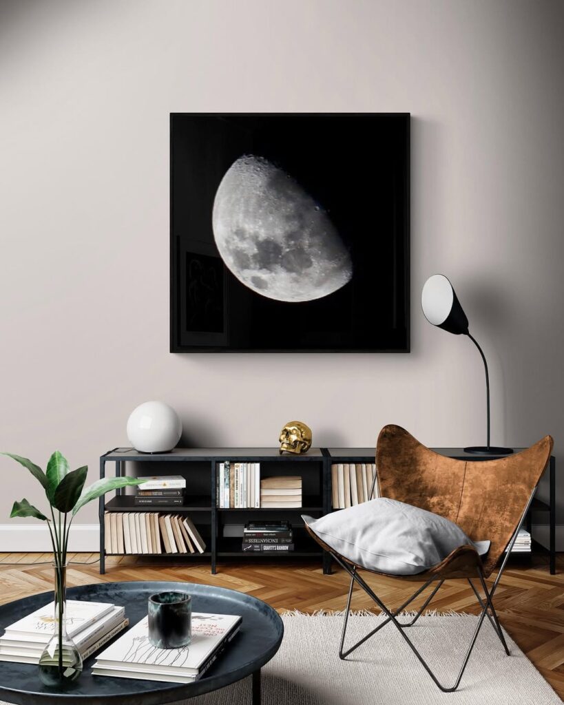 Sala de estar com rack preto com livros, mesa de centro preta e quadro com foto da lua na parede