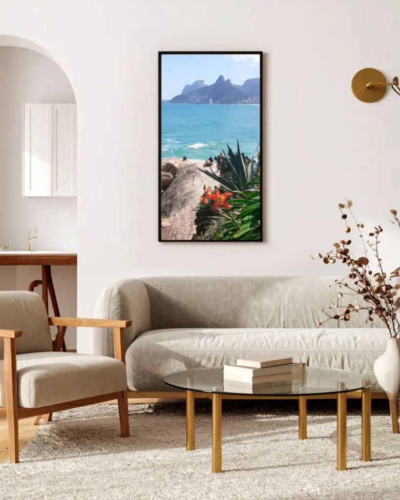 Sala de estar com sofá claro orgânico, mesa de centro com tampo de vidro e quadro com foto colorida de paisagem