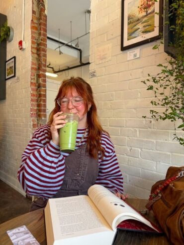Mulher de pele clara, com cabelo ruivo. Ela está tomando um Matcha