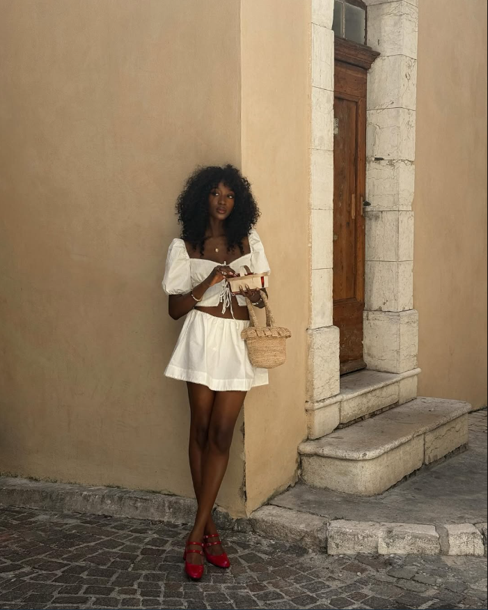 Mulher de pele preta, com look branco e sapato mary jane vermelho 