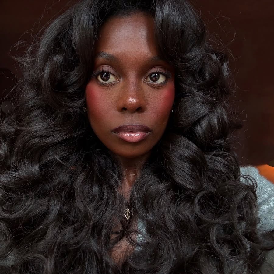 Mulher de pele preta, com cabelo ondulado e maquiagem clean