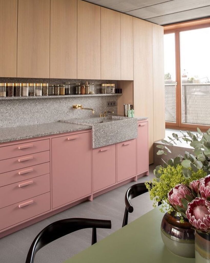 Cozinha com armário inferior rosa e parte superior em tom amadeirado claro, e mesa com tampo verde