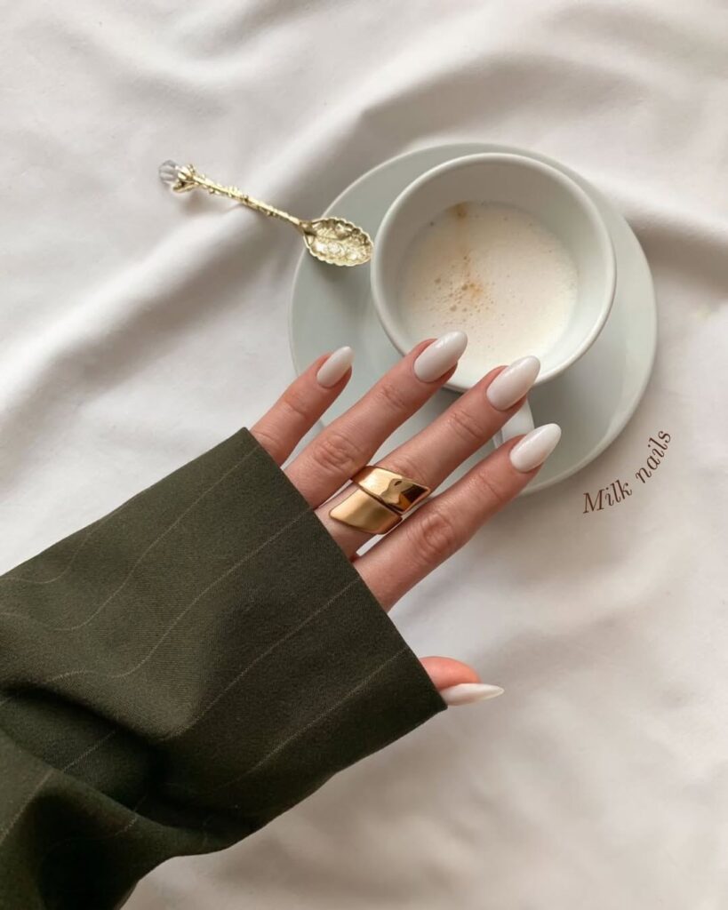 Mão de pele clara, com anel em dourado e unha amendoada milky