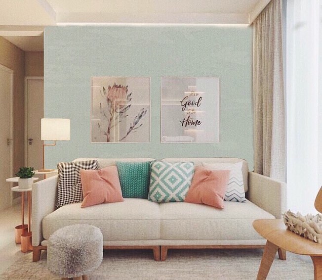 Sala de estar com sofá claro, almofadas coloridas e papel de parede verde com quadros