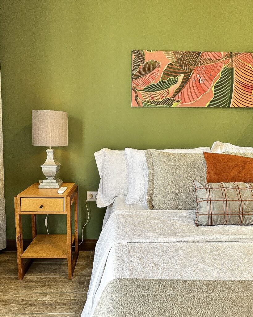 Quarto com parede verde e quadro colorido, mesa de cabeceira de madeira com abajur