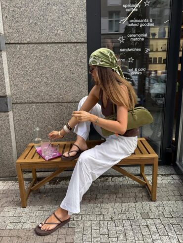 Mulher branca e magra com calça branca, blusa marrom, lenço no cabelo e rasteirinha marrom