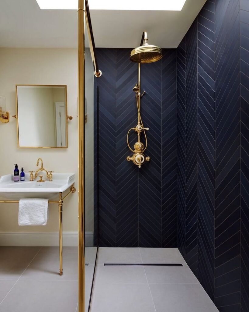 Banheiro com azul na parte do box, chuveiro e detalhes em metal dourado