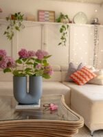 Mesa de centro com linhas orgânicas, tampo de vidro, livro e vaso com design diferenciado e flores rosas