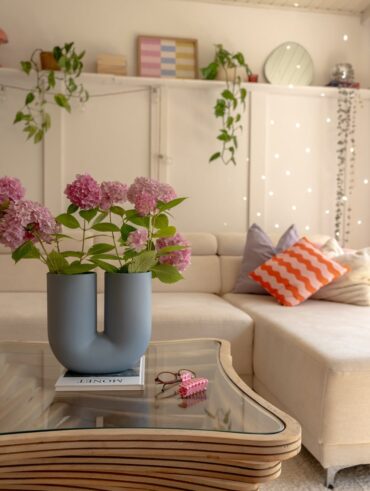 Mesa de centro com linhas orgânicas, tampo de vidro, livro e vaso com design diferenciado e flores rosas