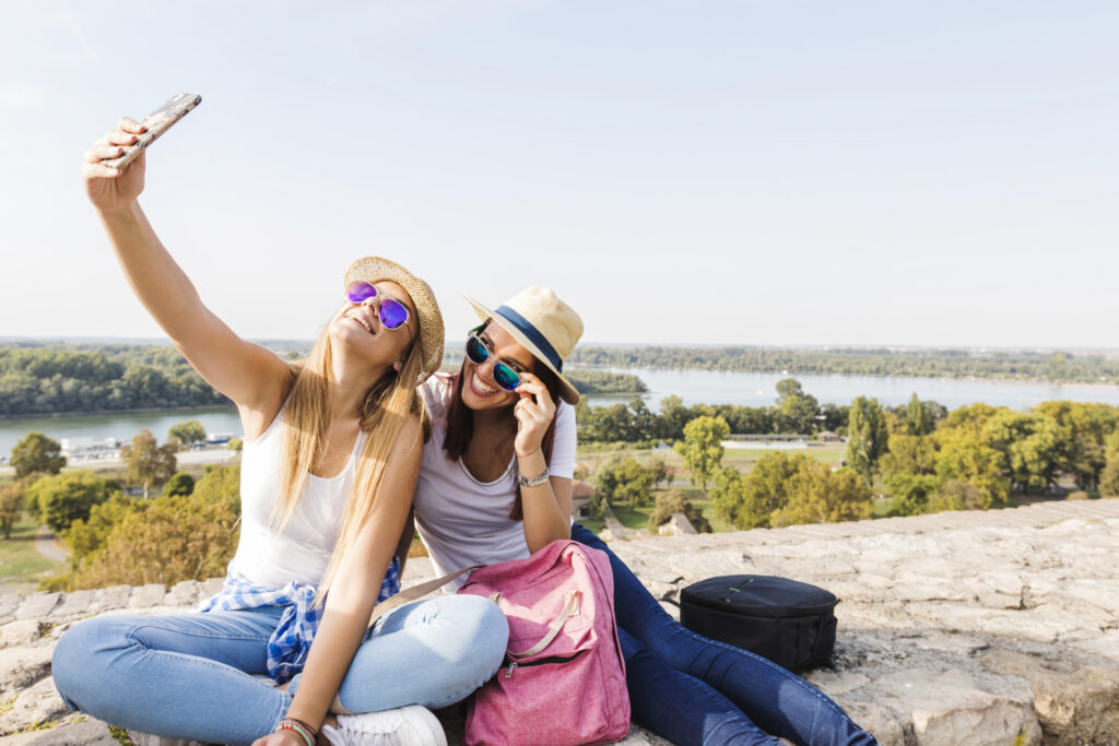 Duas mulheres sentadas em um muro de pedra com óculos de sol e chapéus