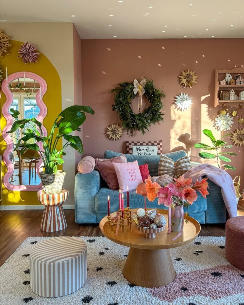 Sala de estar com parede rosa, sofá azul e espelho orgânico