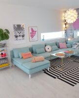 Sala ampla com sofá azul-claro, tapete listrado em branco e preto, mesa de centro com tampo de vidro e luminária com design diferente