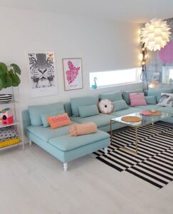 Sala ampla com sofá azul-claro, tapete listrado em branco e preto, mesa de centro com tampo de vidro e luminária com design diferente