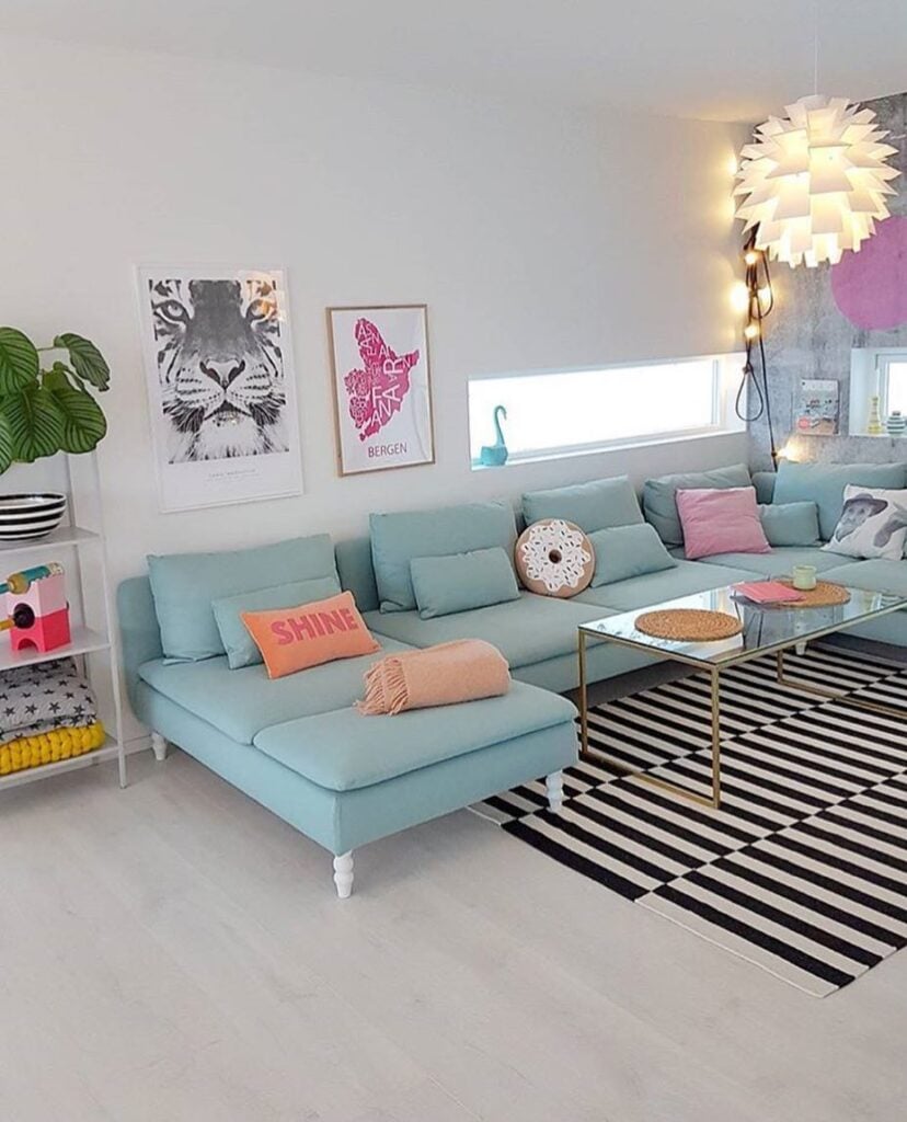 Sala ampla com sofá azul-claro, tapete listrado em branco e preto, mesa de centro com tampo de vidro e luminária com design diferente