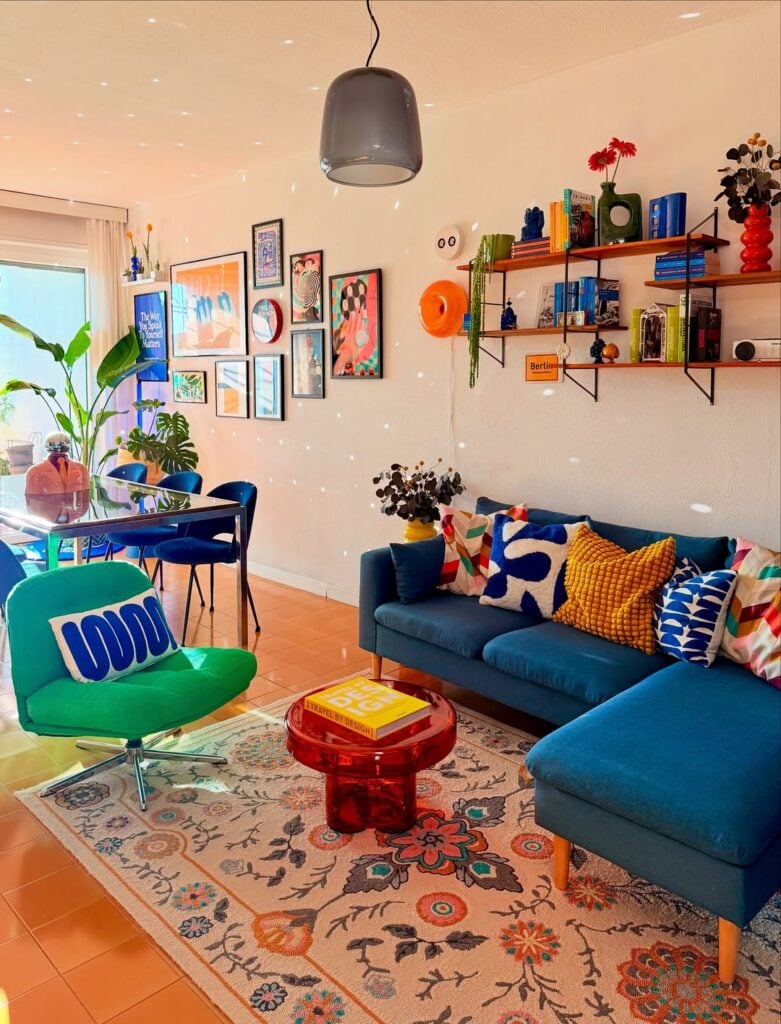 Sala de estar e jantar integradas com sofá azul e pés palito, almofadas coloridas, mesa de centro vermelha e poltrona verde