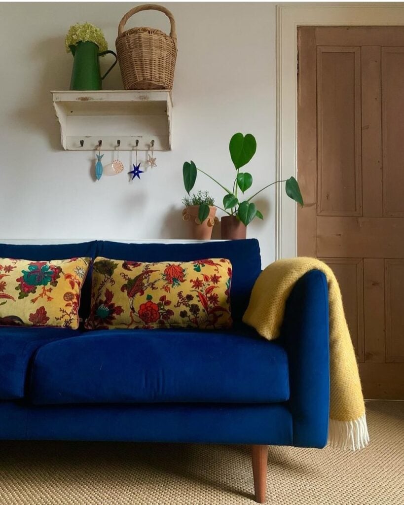 Sofá azul escuro com pés palitos, almofadas amarelas com flores e manta amarela