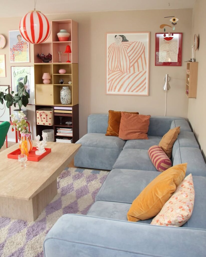 Sala ampla com sofá em L, almofadas coloridas, estante com objetos decorativos e luminária listrada de vermelho e branco