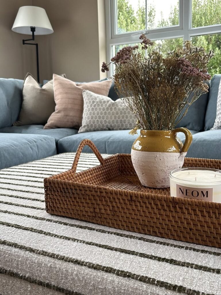 Sala com sofá azul e almofadas, mesa de centro listrada, bandeja decorativa com vela e vaso com flores secas