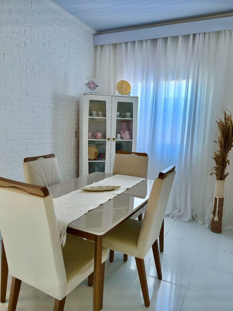Ambiente com mesa retangular, caminho de mesa de crochê e armário branco ao fundo