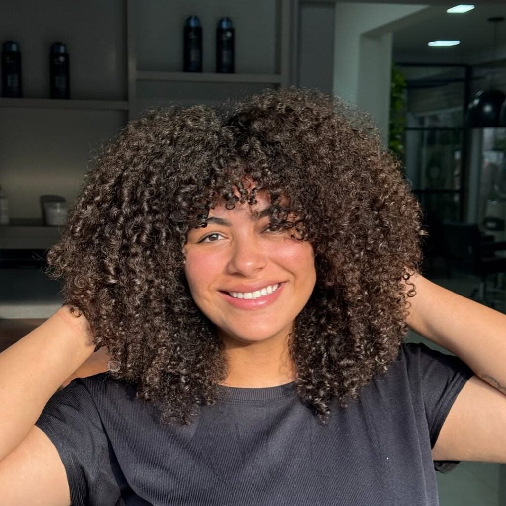 Mulher de pele clara, com blusa escura e cabelo crespo em corte shaggy