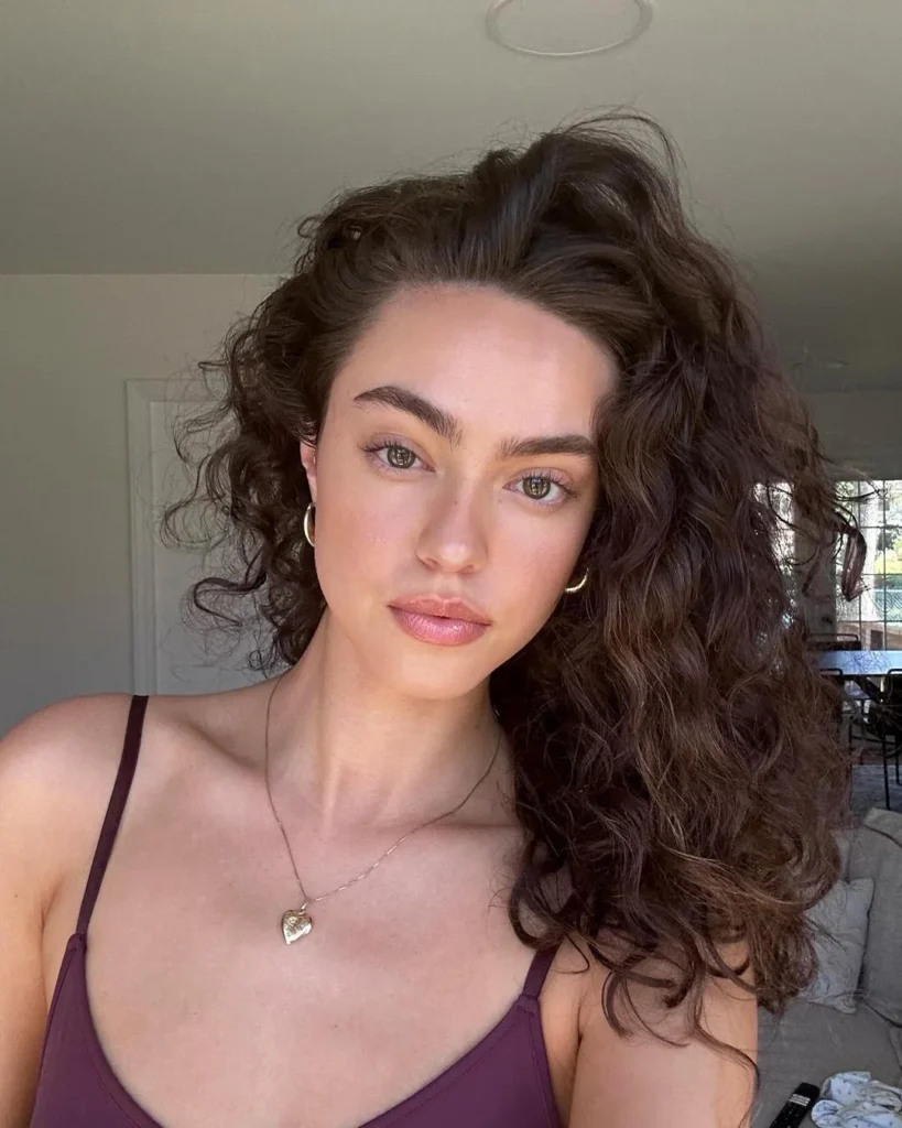 Kiana Davis em foto de rosto. Ela está com o cabelo médio, cacheado e volumoso e usa blusa de alça