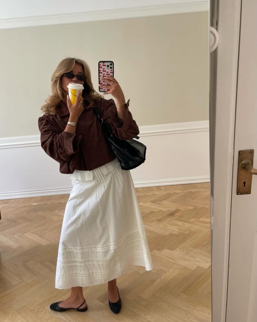 Mulher de pele clara, com saia, camisa comprida e sapatilha slingback