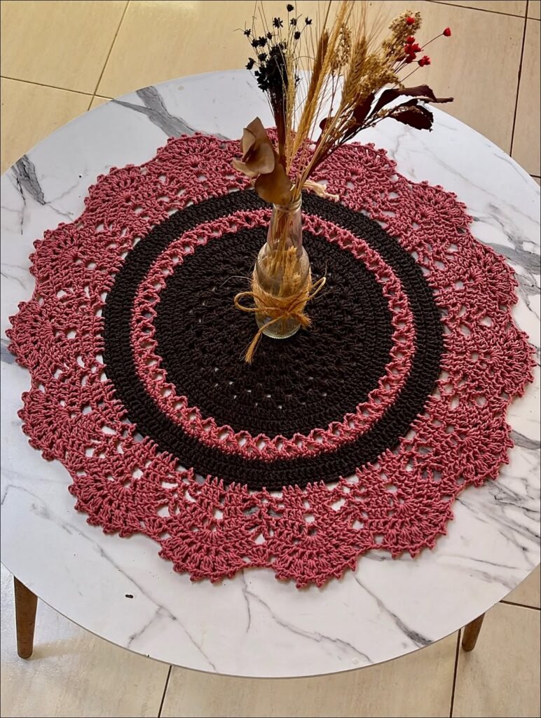 Mesa branca com guardanapo rosa e marrom de crochê e vasinho de flores