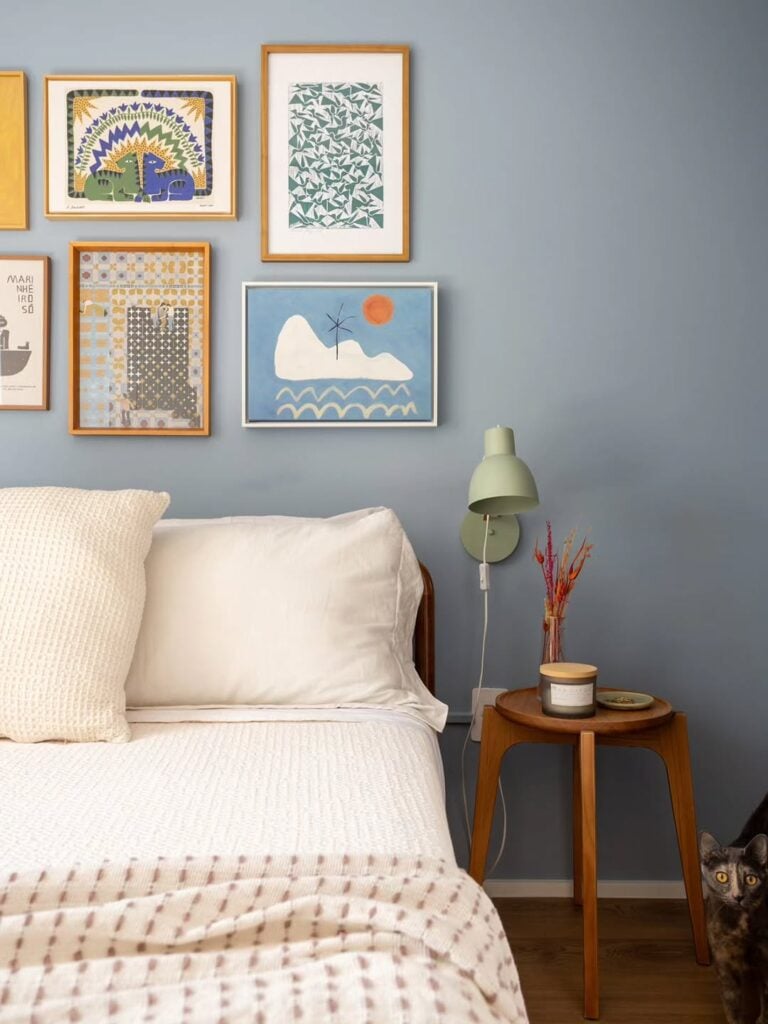 Quarto cpm parede azul, quadros coloridos na parede e mesa de cabeceira de madeira