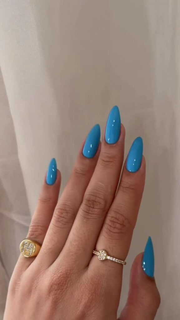 Mão de pele clara, com anel em dourado e unha amendoada azul glacial
