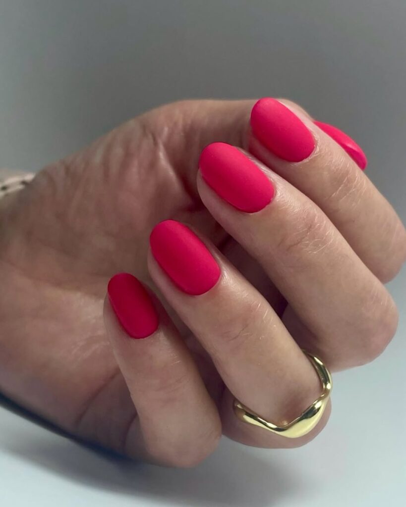 Mão de pele clara, com anel dourado e unha oval rosa matte