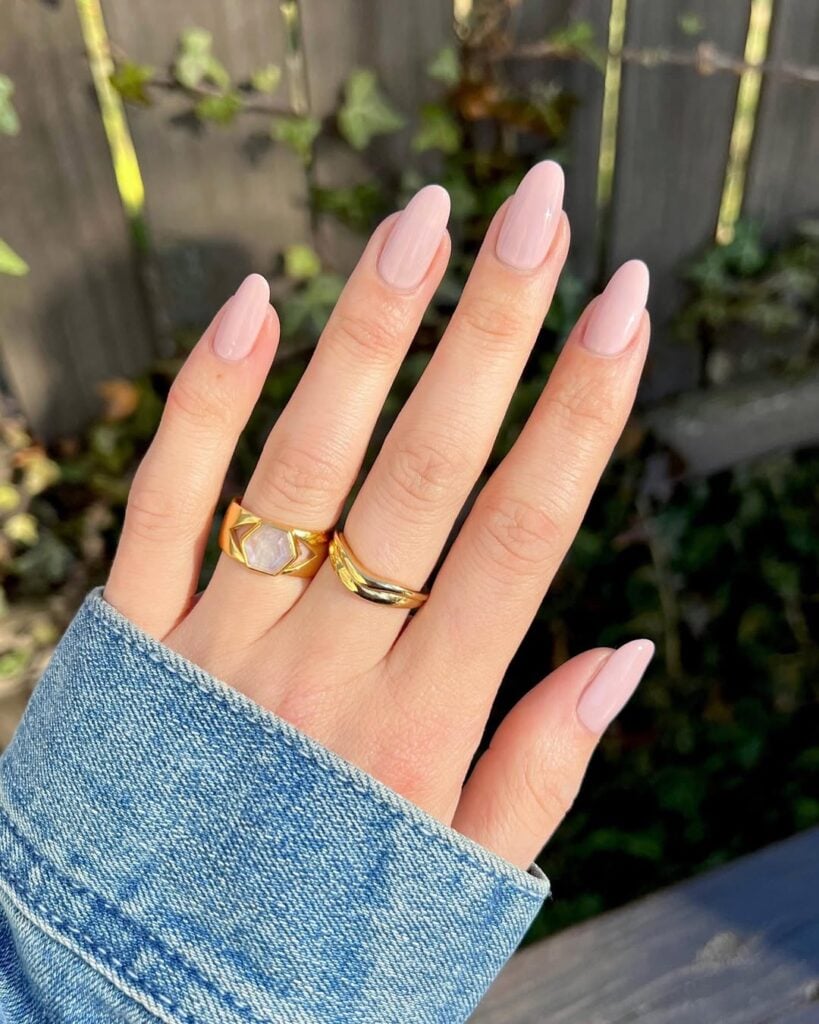 Mão de pele clara, com anéis em dourado e unha amendoada rosa-chá