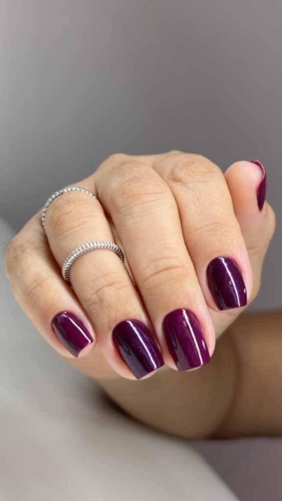 Mão de pele clara, com anel em prata e unha quadrada roxo-escuro